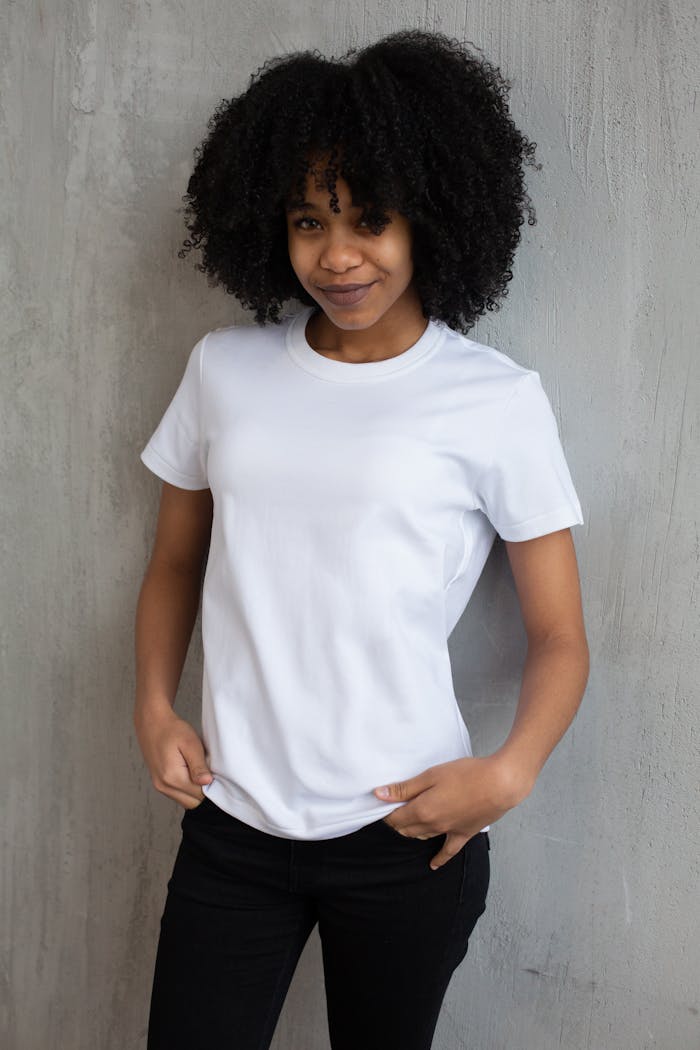 Confident young black woman in casual attire posing against a gray wall in a modern studio setting.